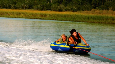Two women slide across water while tubing
